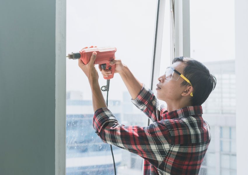 person-repairing-window-frame-with-drill